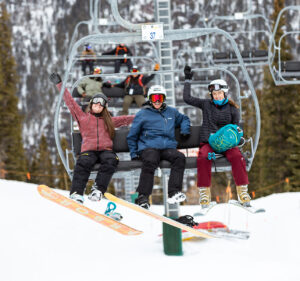 Snowboarding and skiing friends smile on a chairlift in mid-air