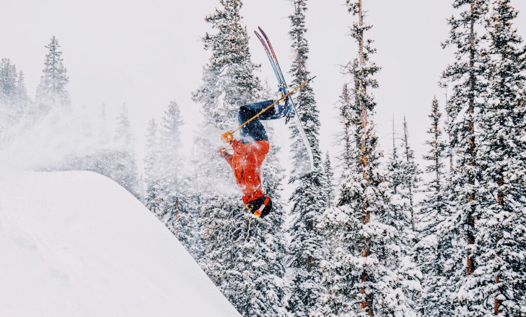 A skier in an orange jacket flips upside down in mid air.