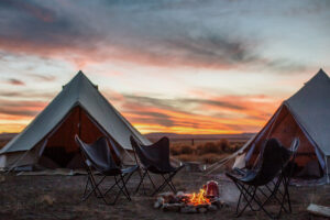 Two bell tents set up on from of a campfire with a red coffee pot.