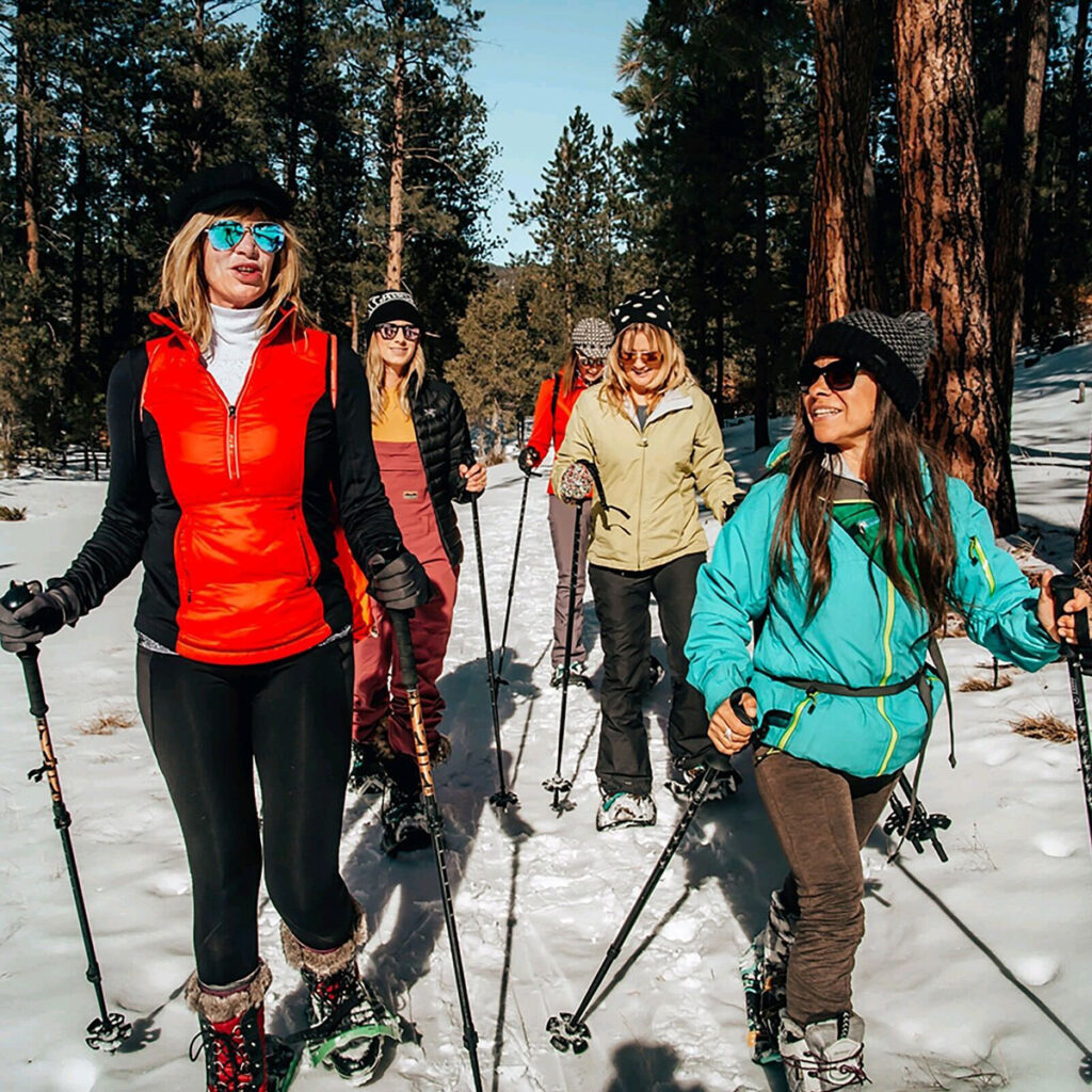 A group of women snowshoe together in brightly colored jackets