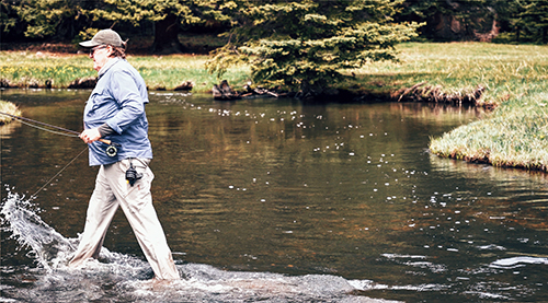 A fly fisherman wades confidently through a mountain stream.