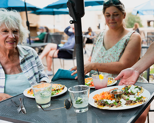 Two women are served food at an outdoor table.