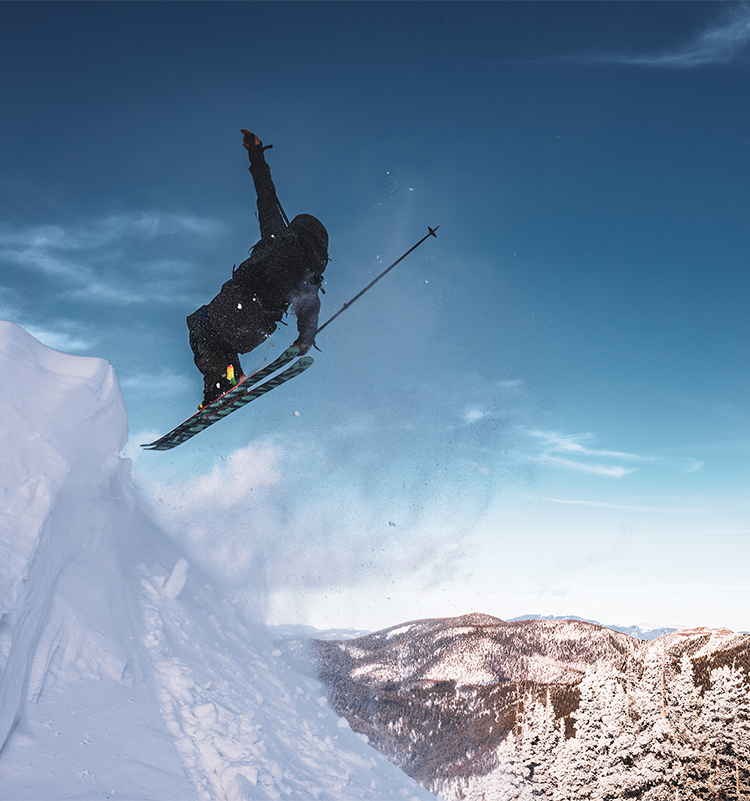 A skier dressed in black spins in mid-air off a snowbank.