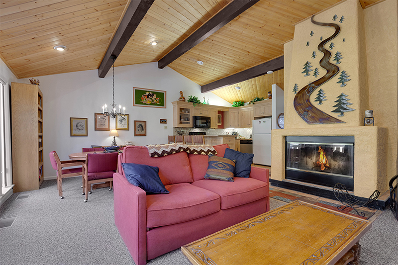 A vaulted ceiling with exposed wooden beams over an open living concept family room with a fireplace.