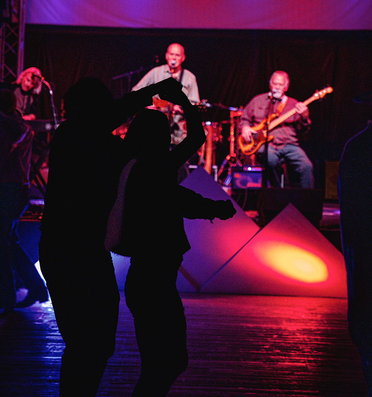 A silhouetted couple dance in front of a band on stage.