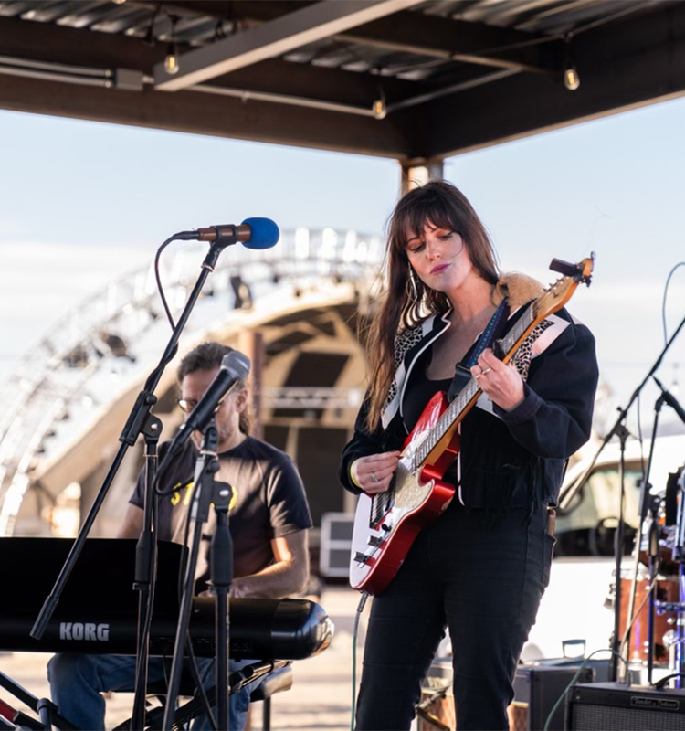 A woman wearing a black leather jacket and black jeans fronts a band playing an electric guitar.