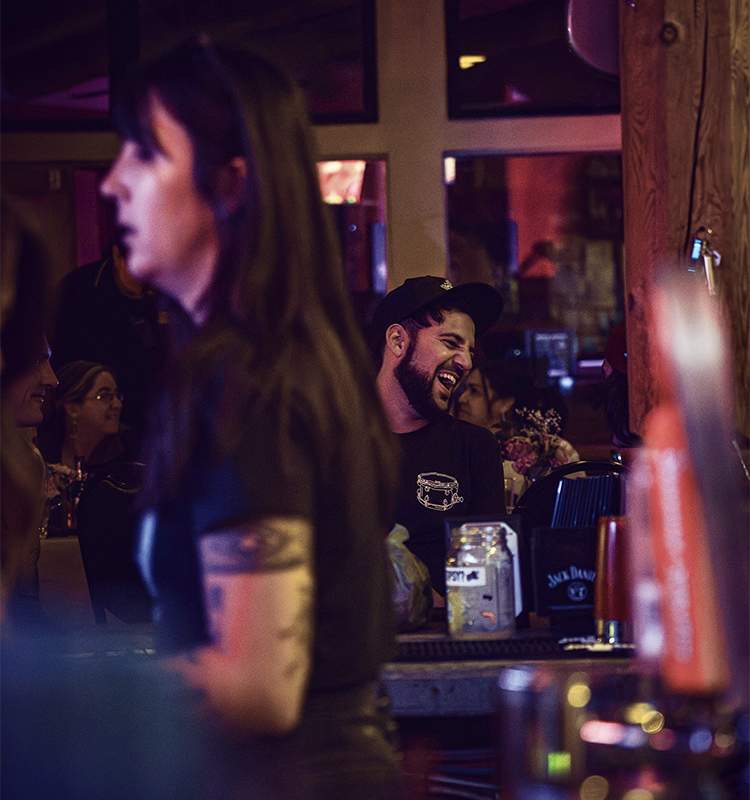 A man smiles and laughs at the end of a crowded bar.