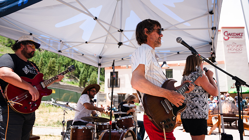 A band plays outdoors under a white tent.