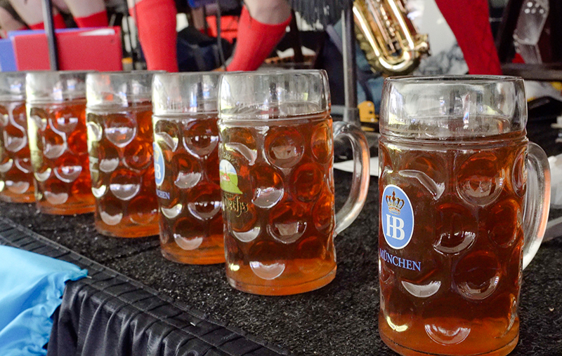 A line of full beer stein sit on the edge of a stage.