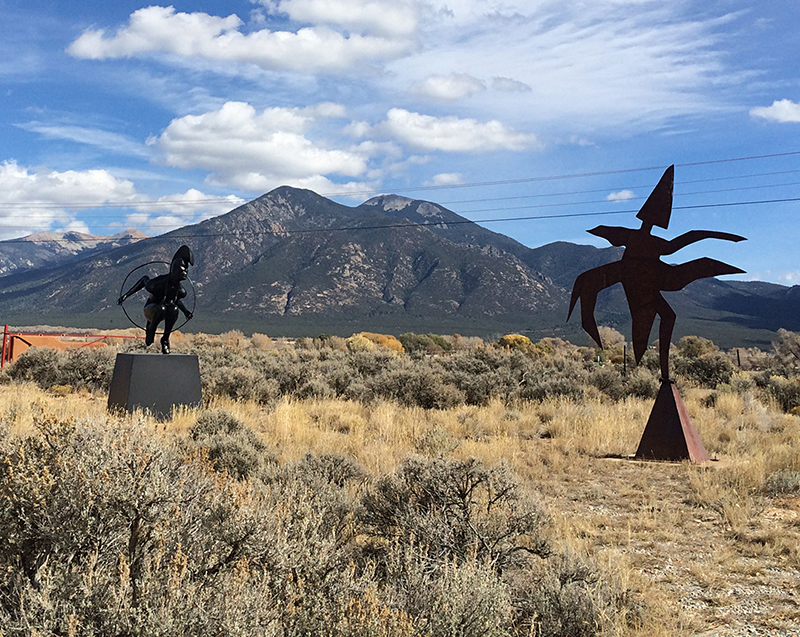 Modern metal sculptures in a yard with a mountain behind.