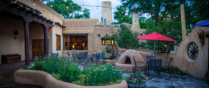 A lush patio surrounded by adobe walls with an outdoor kiva fireplace.