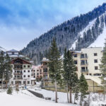 A snowy village of alpine condo buildings sit at the base of a ski slope.