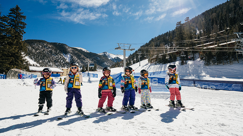 A row of young kids learning how to ski.