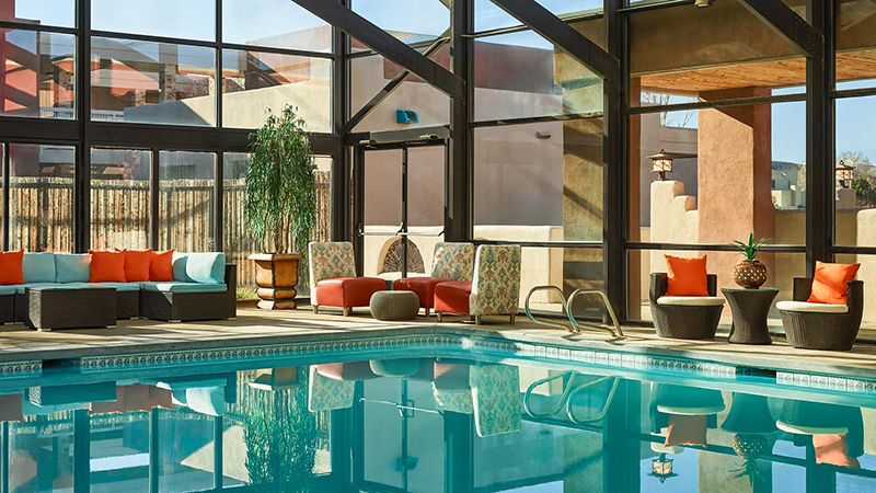 An indoor pool in a greenhouse with colorful orange and turquoise poolside seating.