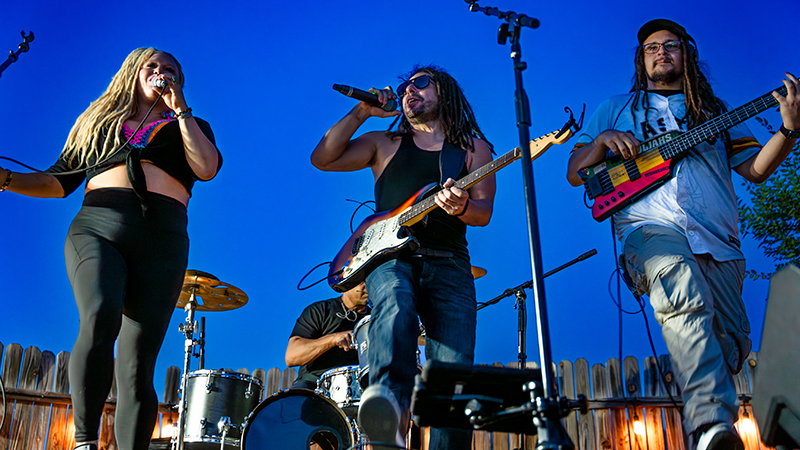 A band performs on an outdoor stage with blue sky behind them.