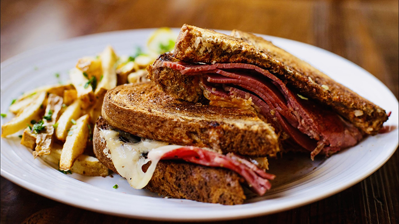 A Reuben sandwich and fries on a white plate.