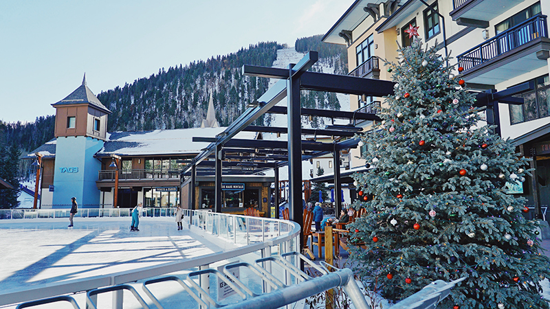 A Christmas tree wits at the edge of an outdoor ice skating rink in the mountains.