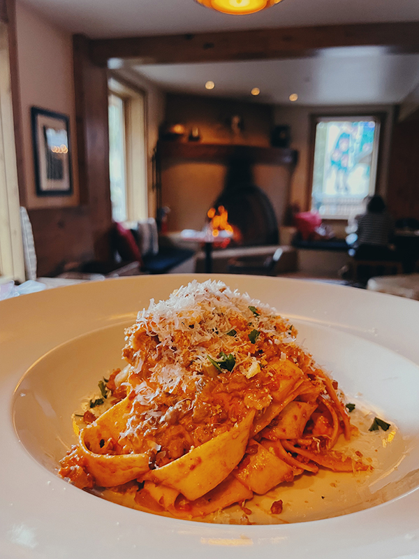 A plate of pasta sits in front of a cozy fireplace in a restaurant.