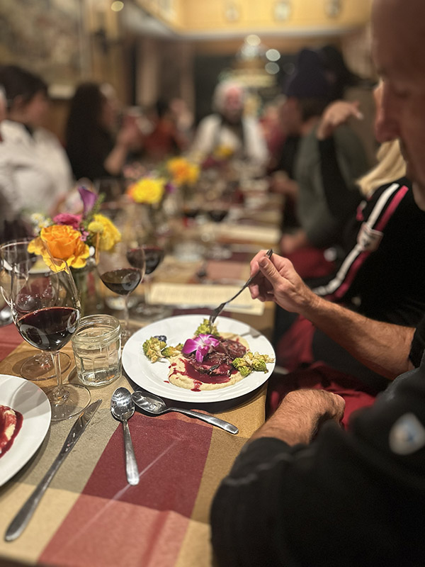A man seated at a long table gathers a bite of food on a fork.