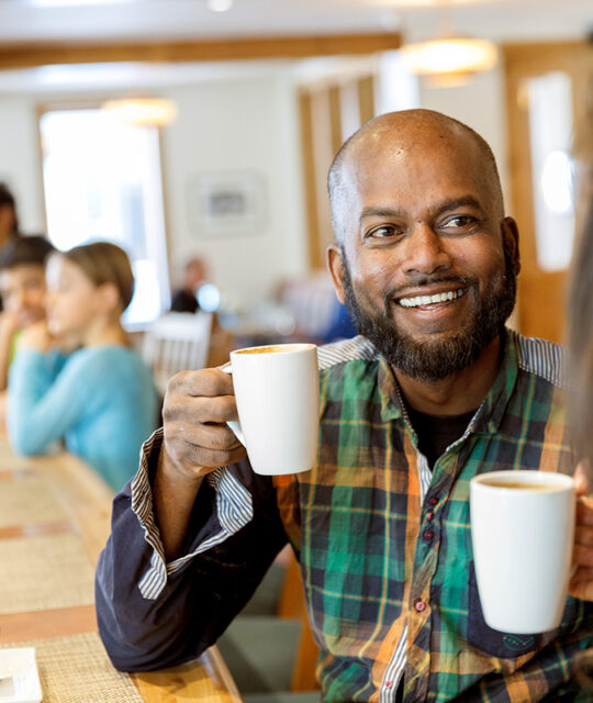 A man smiles with a cup of coffee