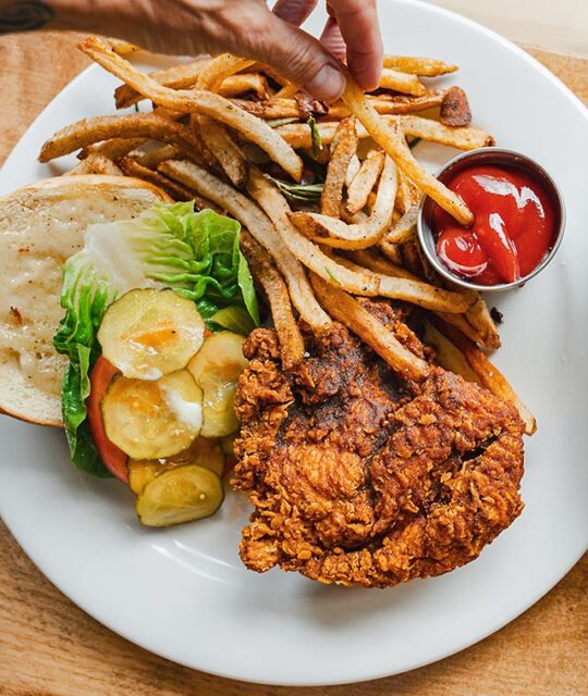 Fried chicken sandwich, pickles and fries being dipped in catsup