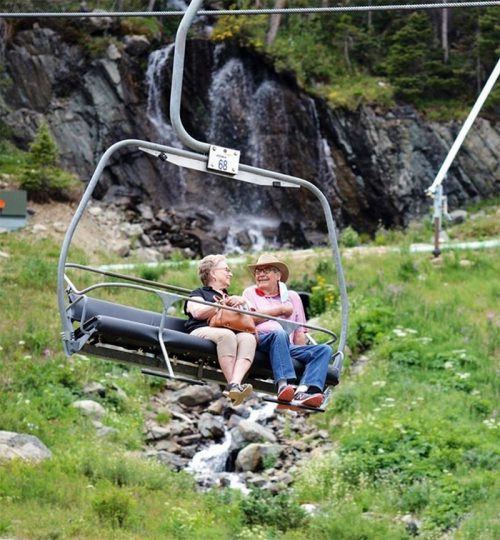 An older couple smile at each other riding the lift past a waterfall in Taos Ski Valley