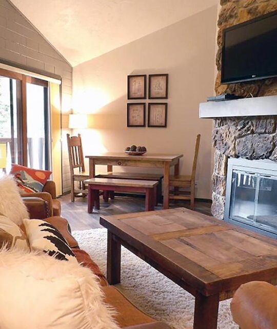 A great room with a stone fireplace and family style dining table.