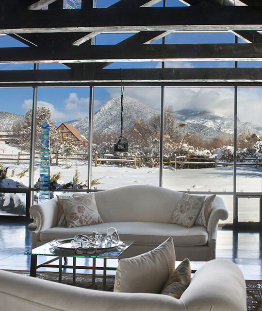 Living room of home in Arroyo Seco looking out on a snowy landscape and mountains.