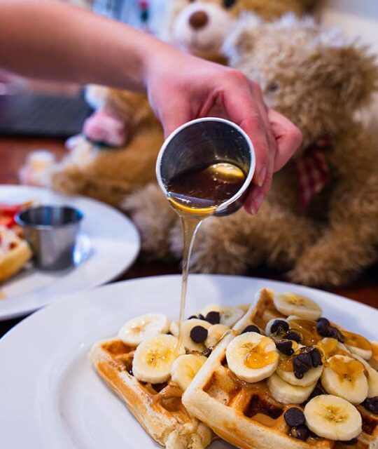 Server pouring maple syrup over banana chocolate chip waffles.