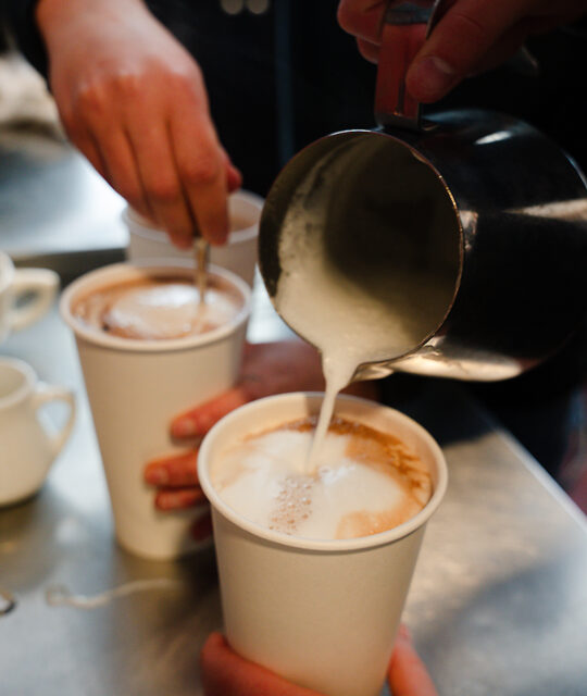 Pouring frothed milk into a coffee to go.