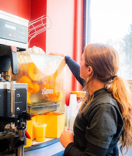 Woman working a fresh squeezed orange juice machine.