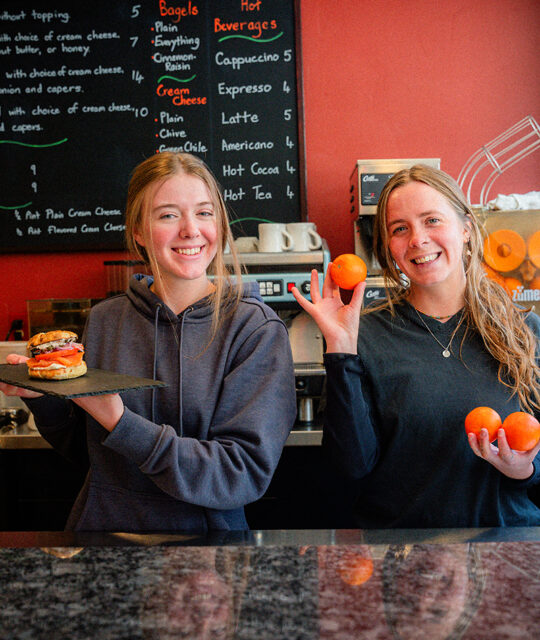 Happy servers holding a bagel and orange.