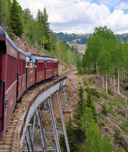 Historic steam train crossing a trestle in the mountains.