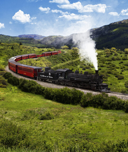 Steam train rounding a corner in scenic mountains