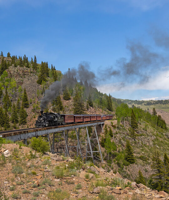 Historic steam train crossing a trestle in the mountains.