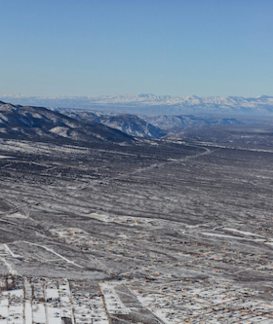 View of snowy mesa with mountains in the distance.
