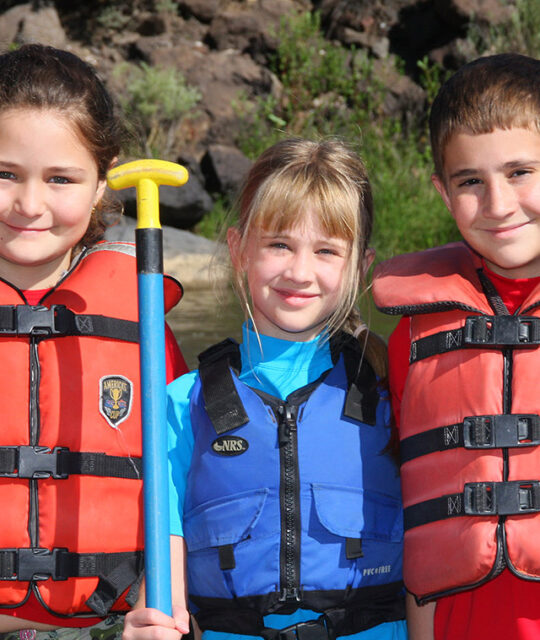 Three kids in rafting life jackets and paddles