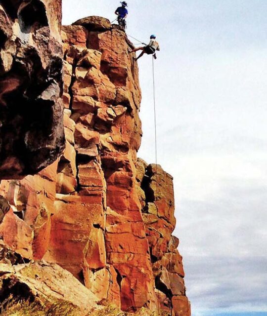 Climber rappelling off cliff with Far Flung Adventures rock climbing guides.