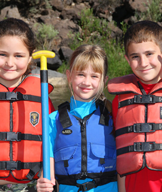Three kids in rafting life jackets and paddles