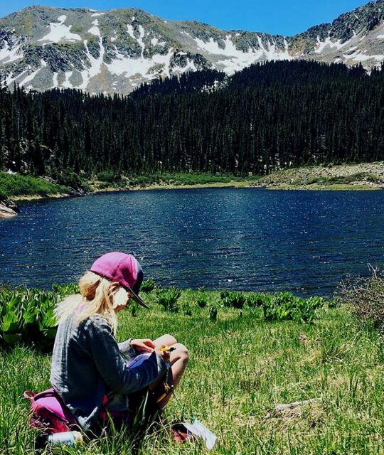 Girl in the green grass drawing at Williams Lake with the Field Institute of Taos summer camp hike.