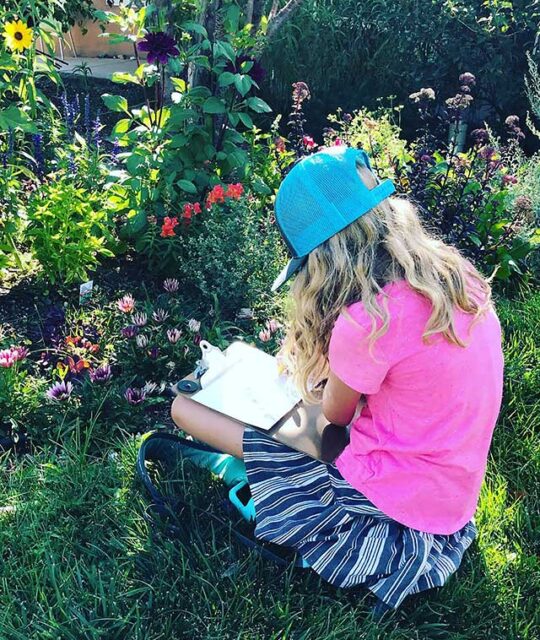 Girl in pink t-shirt and blue cap drawing flowers.