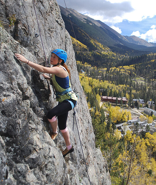 Girl rock climbing in Taos Ski Valley with Fall colors and Wheeler Peak in background