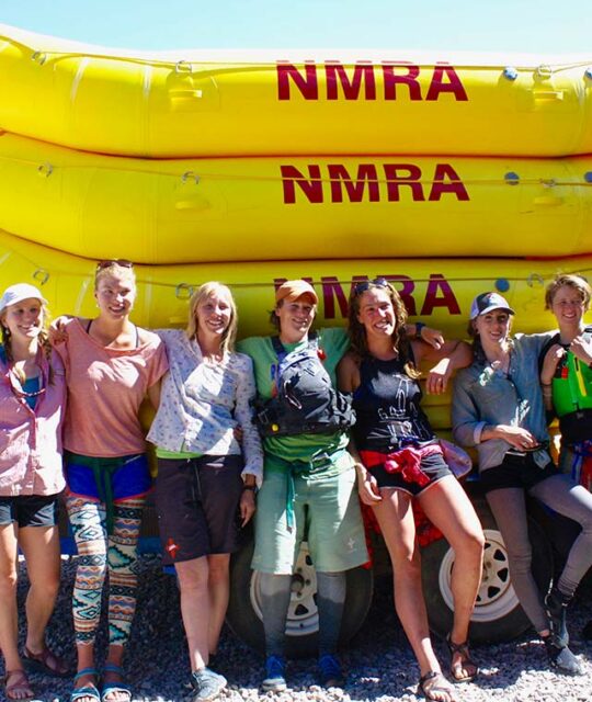 A group of rafting guides standing in front of a stack of yellow NMRA rafts.