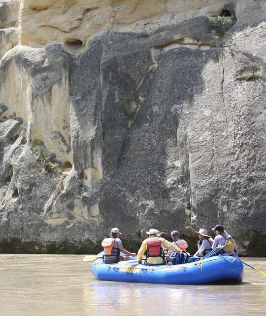 River rafting float trip in calm waters next to canyon wall.