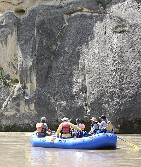 River raft in calm waters next to canyon wall