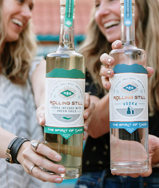 Smiling women with Rolling Still infused vodka bottles