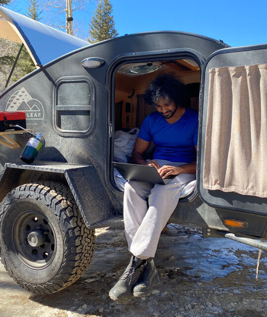 Man on laptop sitting in small camper in the winter sun.