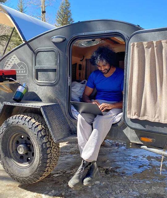 Man on laptop sitting in small camper in the winter sun.