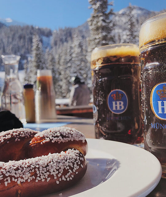 Winter scene with snowy mountain and tall steins of German beer and pretzel.