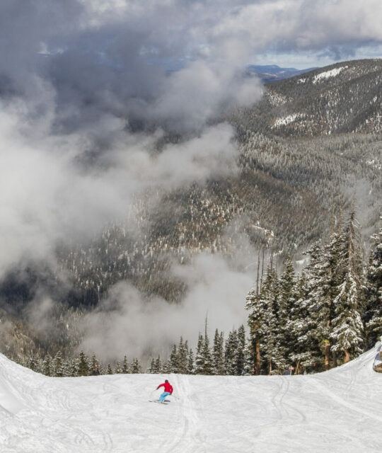 A lone skier on an open run with low clouds in the air